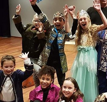 Een groep kinderen in theater costuums. Prins, Prinses, soldaat, lakij. Zij hebben hun handen in de lucht en lachen